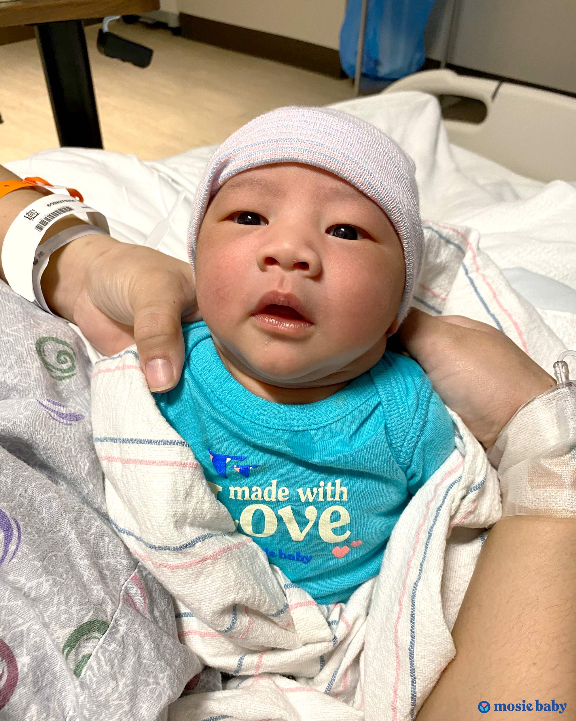 A newborn baby in a Mosie onesie and beanie hat