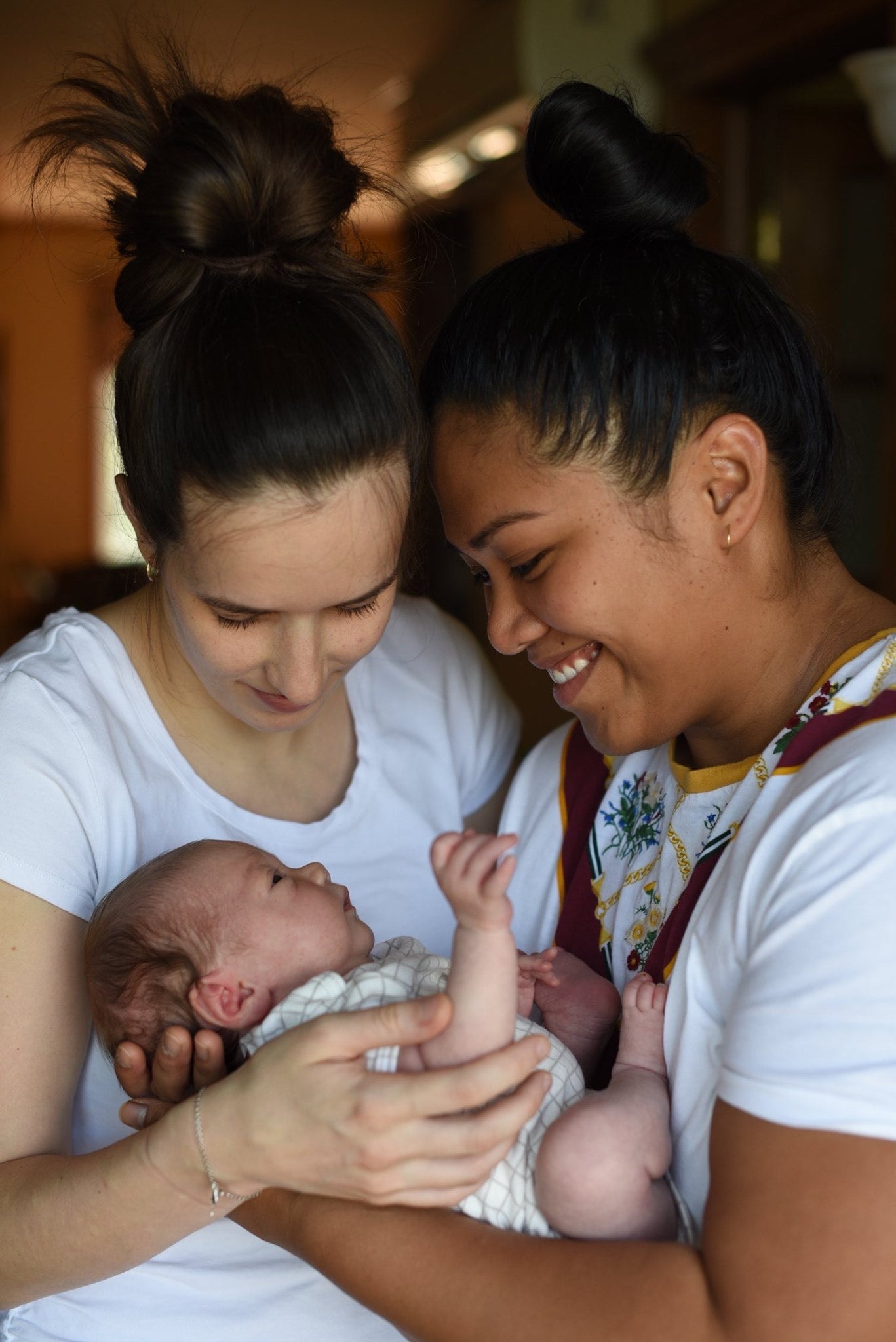 newborn mosie baby being held and admired by moms in white shirts